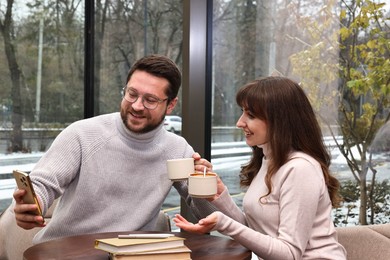 Happy colleagues with smartphone having coffee break at wooden table in cafe