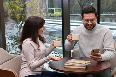 Happy colleagues having coffee break at wooden table in cafe