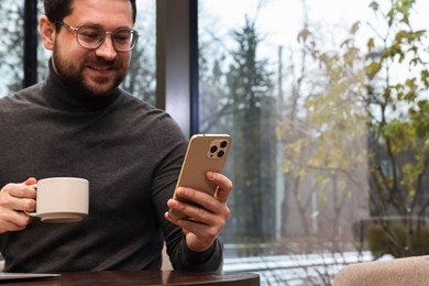 Photo of Smiling businessman with smartphone having coffee break in cafe. Space for text