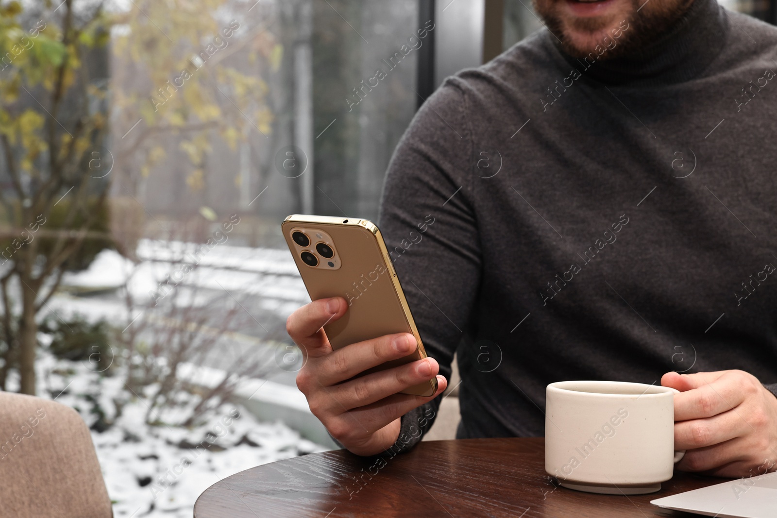 Photo of Businessman with smartphone having coffee break at wooden table in cafe, closeup. Space for text