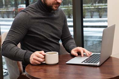 Photo of Businessman with laptop having coffee break at wooden table in cafe, closeup