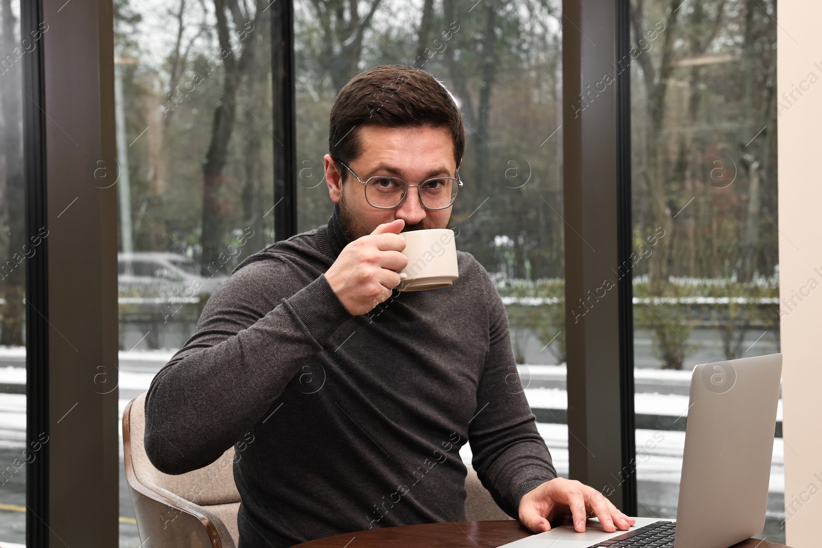 Photo of Businessman with laptop having coffee break at wooden table in cafe