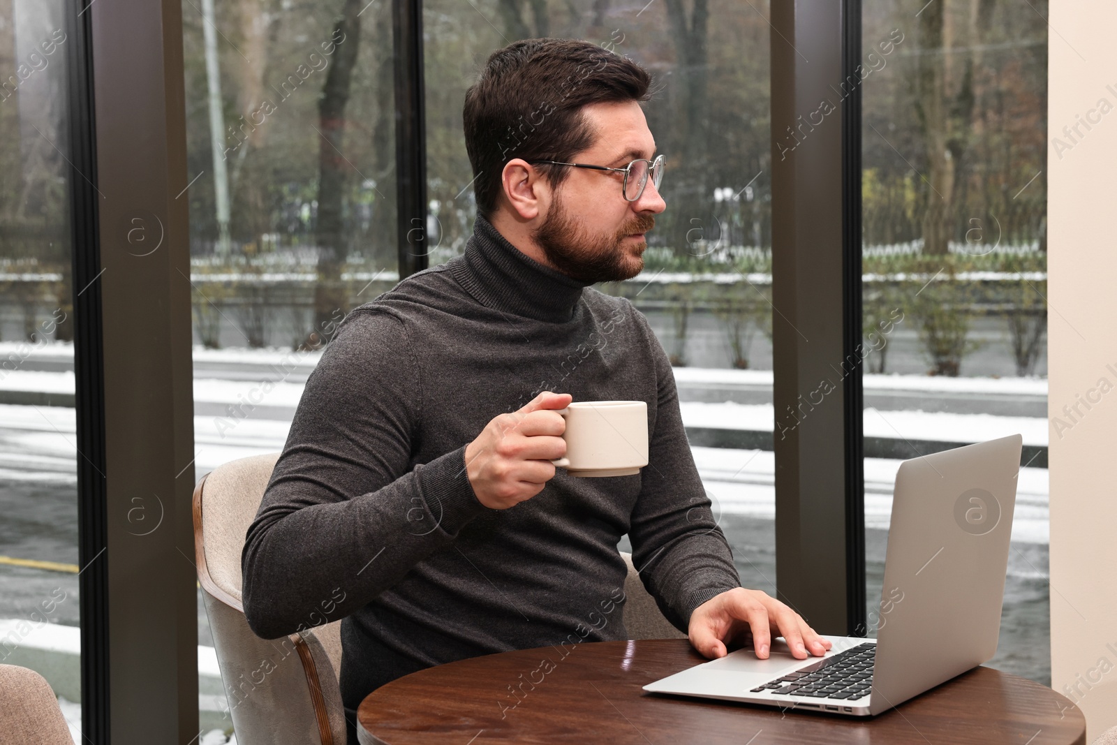 Photo of Businessman with laptop having coffee break at wooden table in cafe