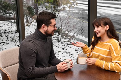 Photo of Happy colleagues talking during coffee break at wooden table in cafe