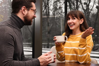 Photo of Happy colleagues talking during coffee break at wooden table in cafe