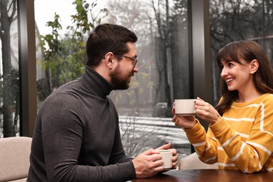 Happy colleagues talking during coffee break at wooden table in cafe