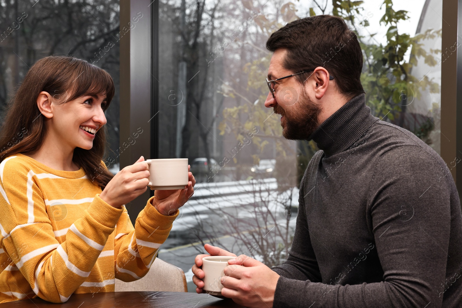 Photo of Happy colleagues talking during coffee break at wooden table in cafe