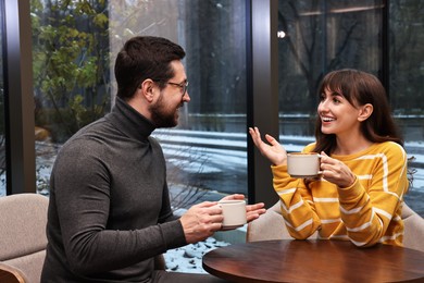 Happy colleagues talking during coffee break at wooden table in cafe