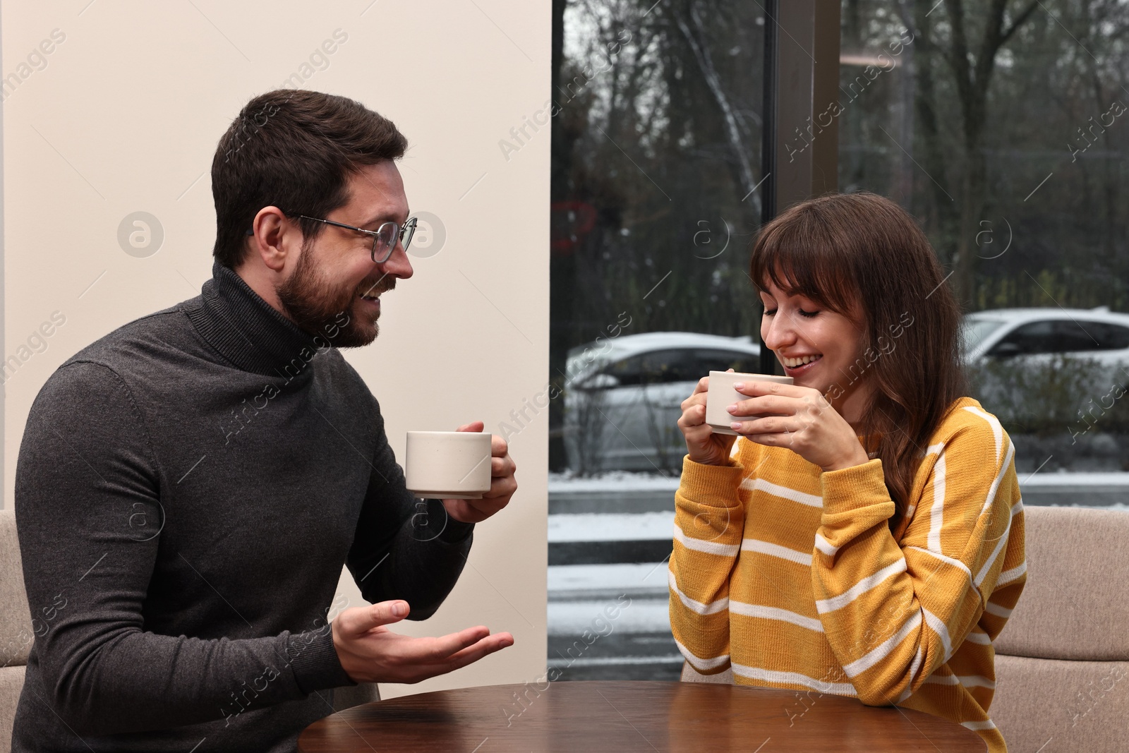 Photo of Happy colleagues talking during coffee break at wooden table in cafe