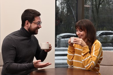 Photo of Happy colleagues talking during coffee break at wooden table in cafe