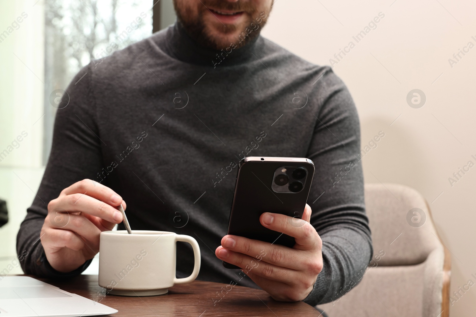 Photo of Man with smartphone having coffee break at wooden table in cafe, closeup