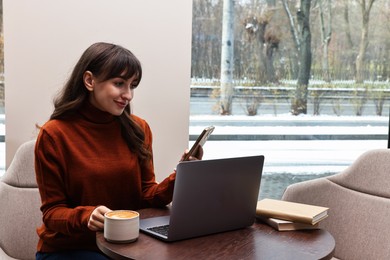 Photo of Beautiful woman with smartphone having coffee break at wooden table in cafe