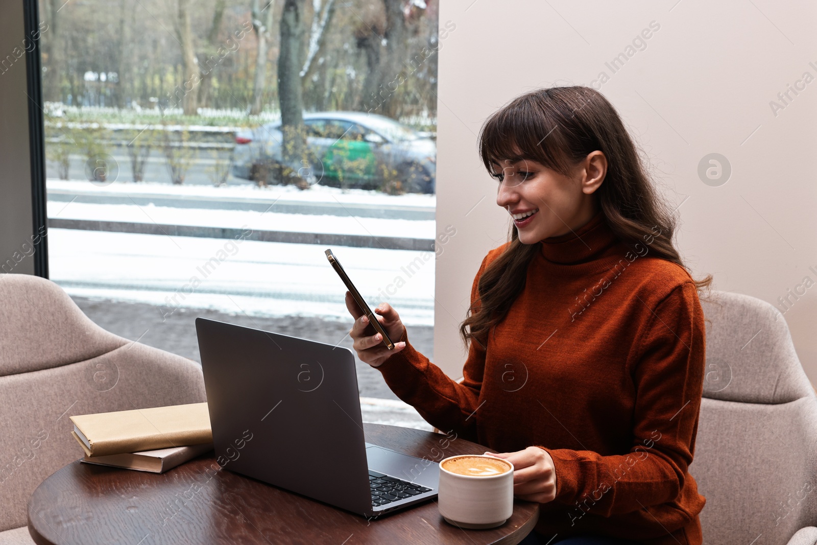 Photo of Smiling woman with smartphone having coffee break at wooden table in cafe