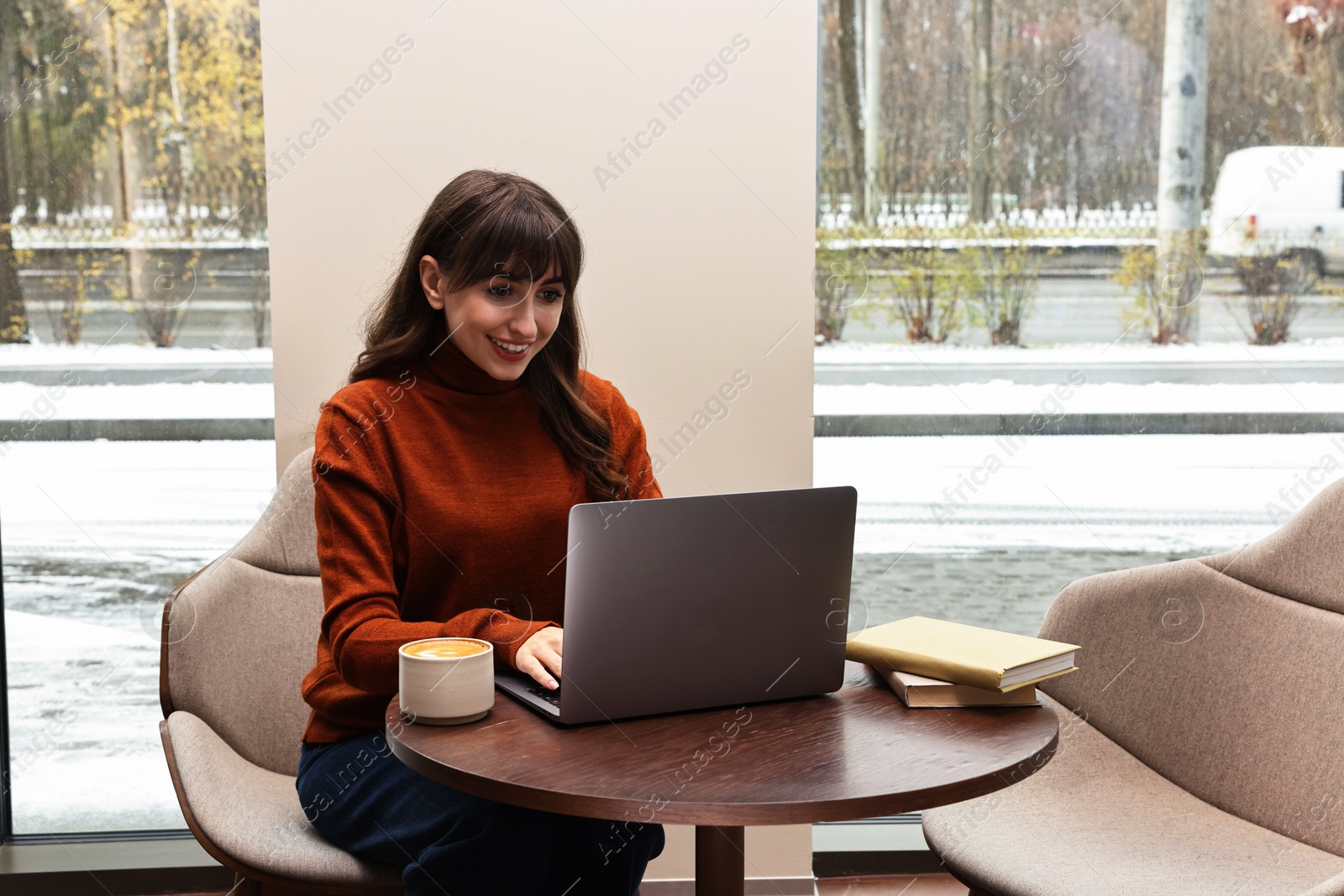 Photo of Smiling woman with laptop having coffee break at wooden table in cafe