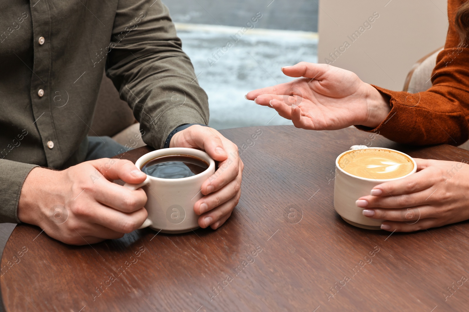 Photo of Colleagues having coffee break at wooden table in cafe, closeup