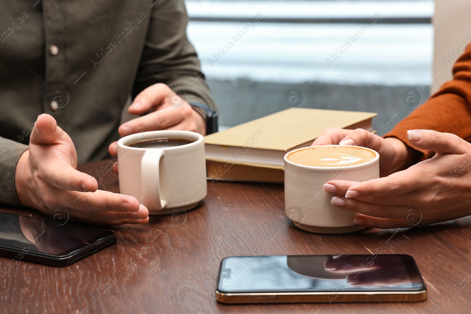 Photo of Colleagues having coffee break at wooden table in cafe, closeup