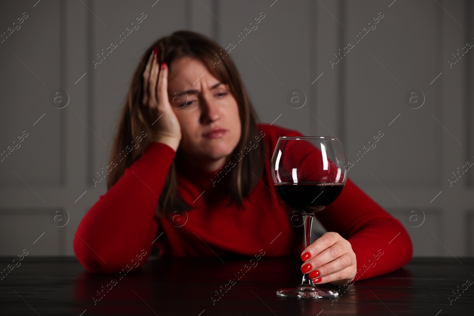 Photo of Alcohol addiction. Woman with glass of red wine at wooden table indoors, selective focus