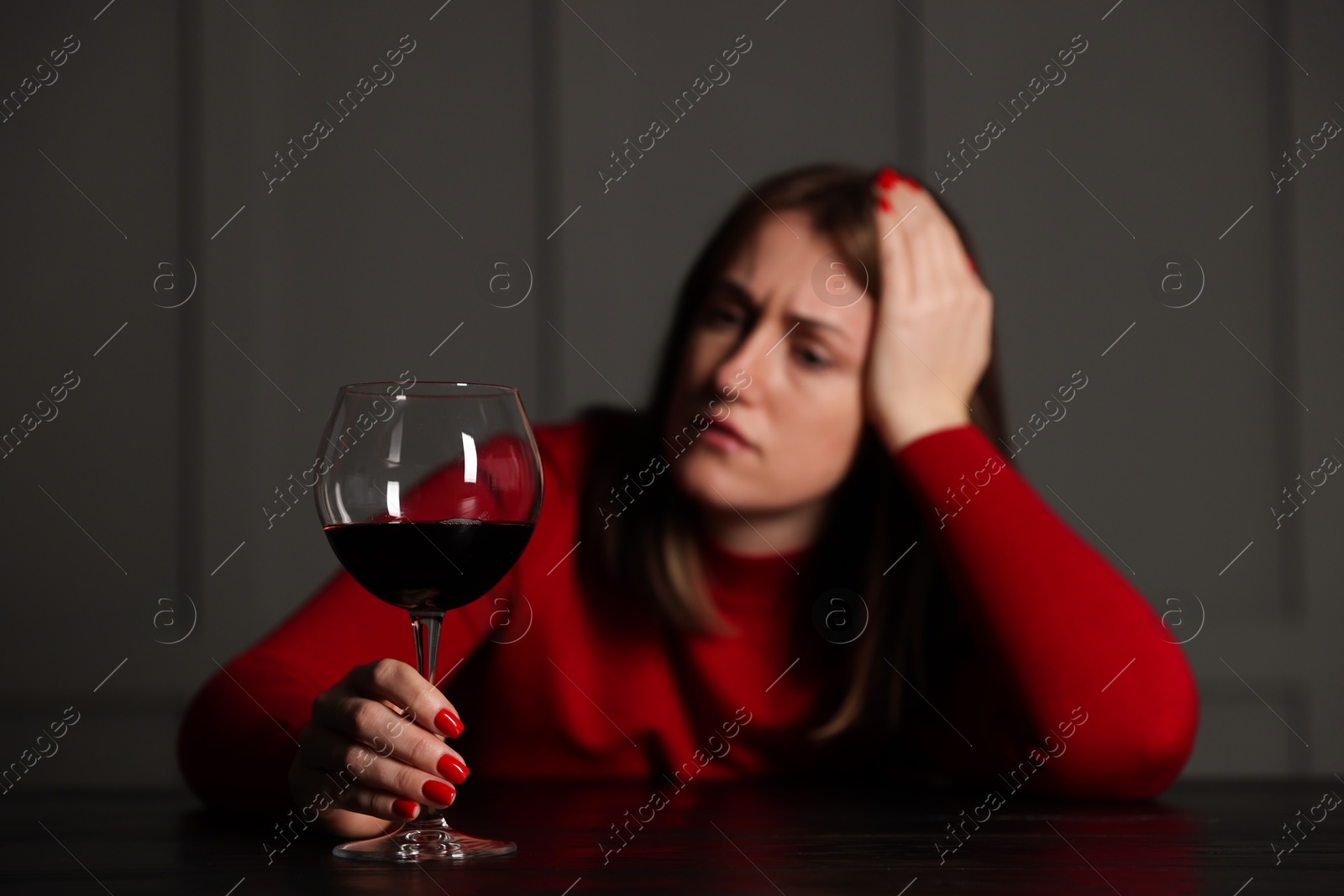 Photo of Alcohol addiction. Woman with glass of red wine at wooden table indoors, selective focus