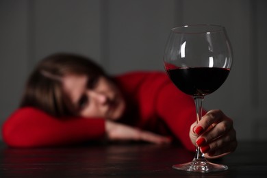 Photo of Alcohol addiction. Woman with glass of red wine at wooden table indoors, selective focus