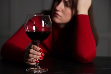 Photo of Alcohol addiction. Woman with glass of red wine at wooden table indoors, selective focus