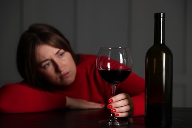 Photo of Alcohol addiction. Woman with glass of red wine and bottle at wooden table indoors, selective focus