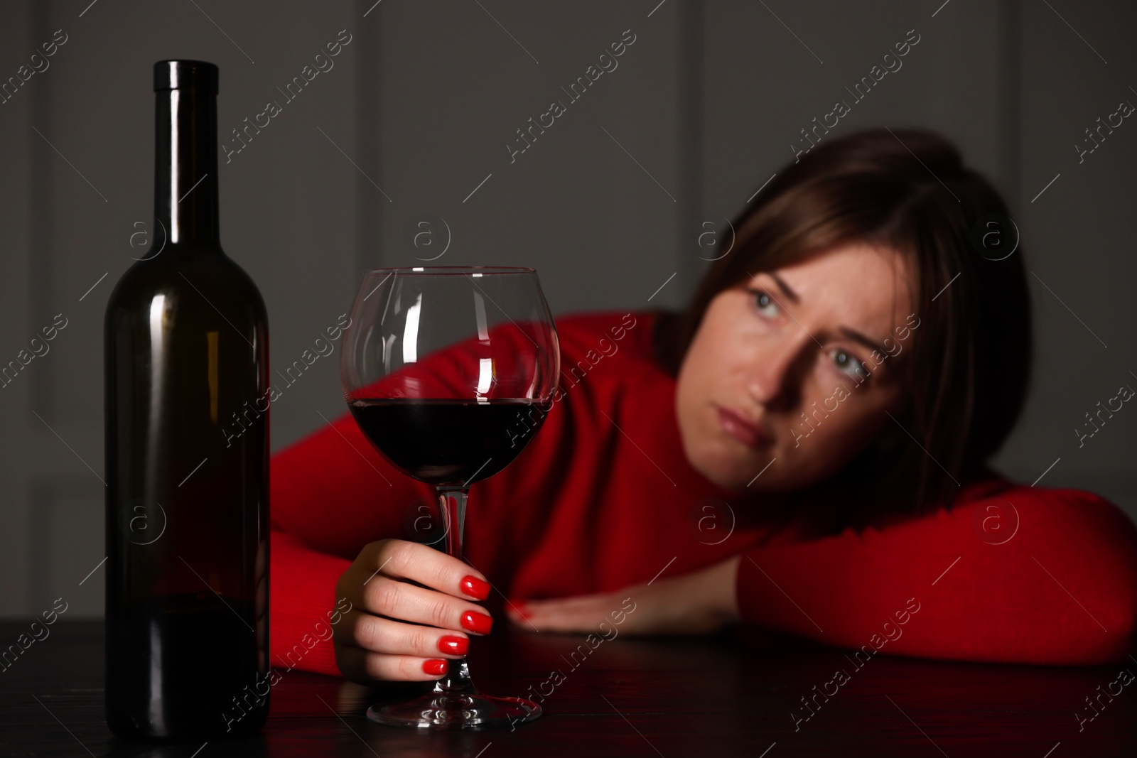 Photo of Alcohol addiction. Woman with glass of red wine and bottle at wooden table indoors, selective focus