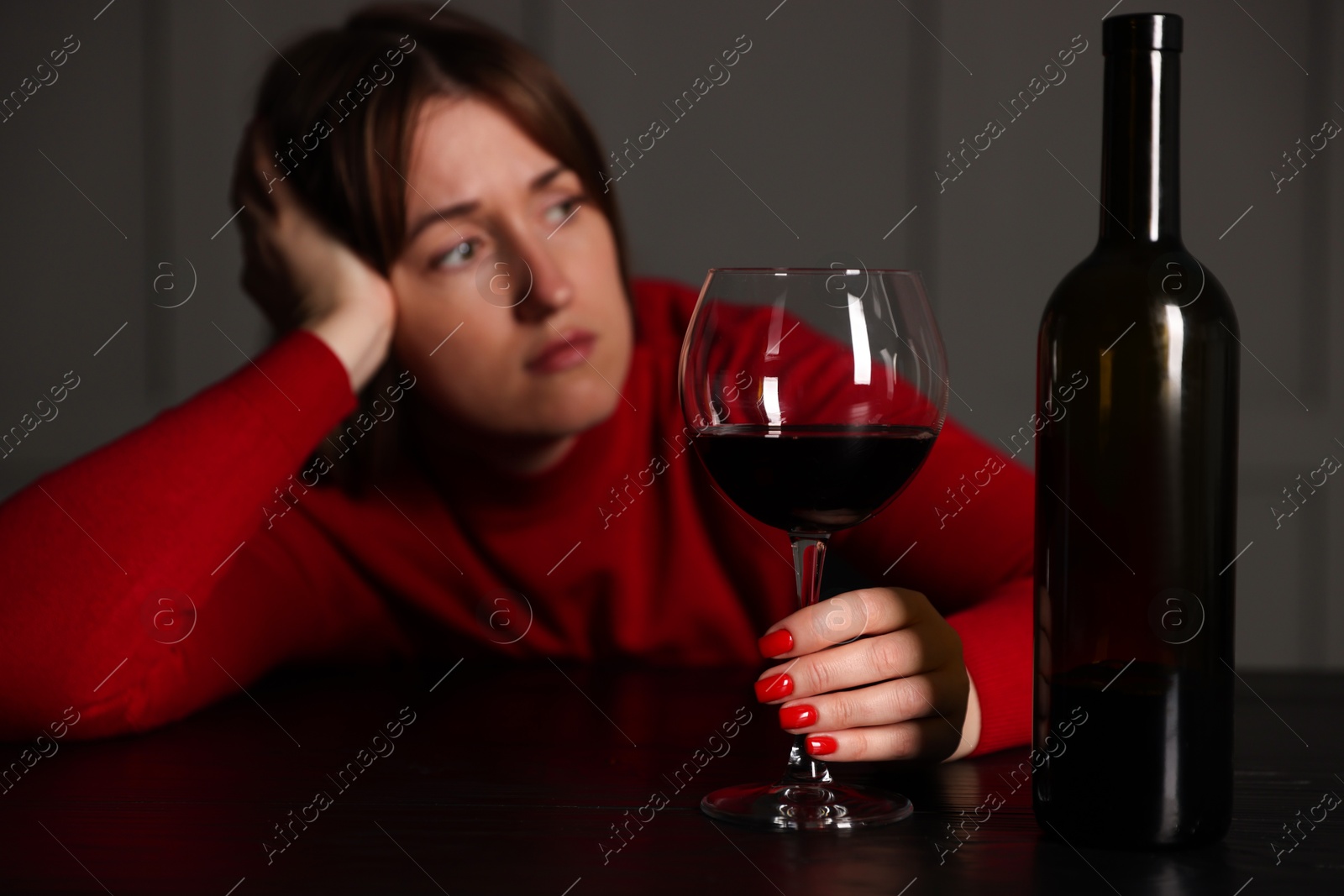 Photo of Alcohol addiction. Woman with glass of red wine and bottle at wooden table indoors, selective focus