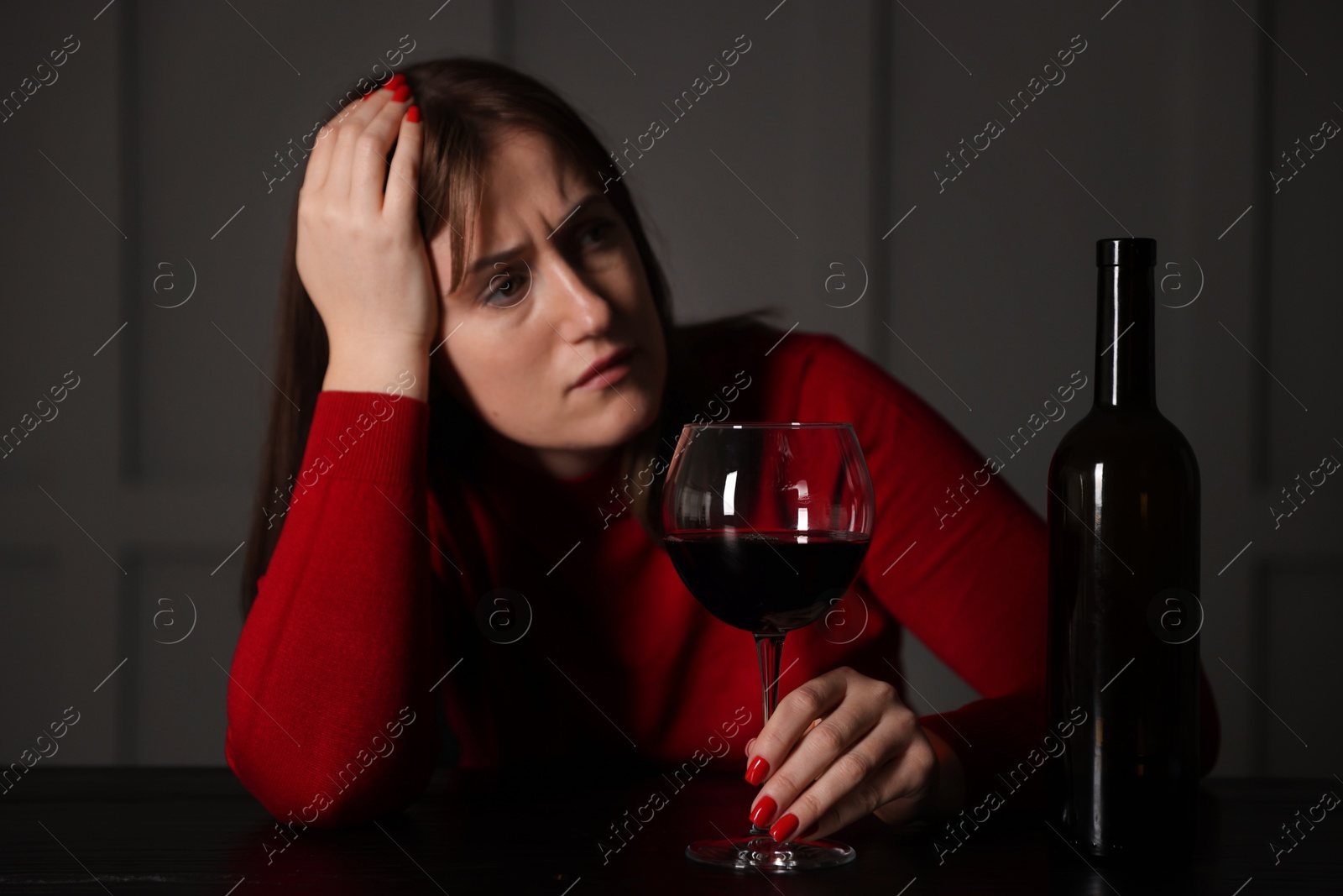 Photo of Alcohol addiction. Woman with glass of red wine and bottle at wooden table indoors