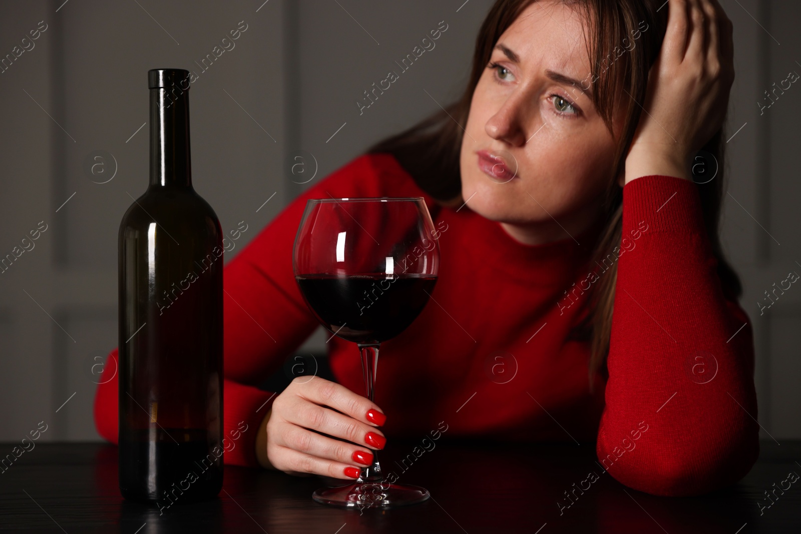 Photo of Alcohol addiction. Woman with glass of red wine and bottle at wooden table indoors