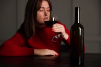 Photo of Alcohol addiction. Woman drinking red wine at table indoors, focus on bottle