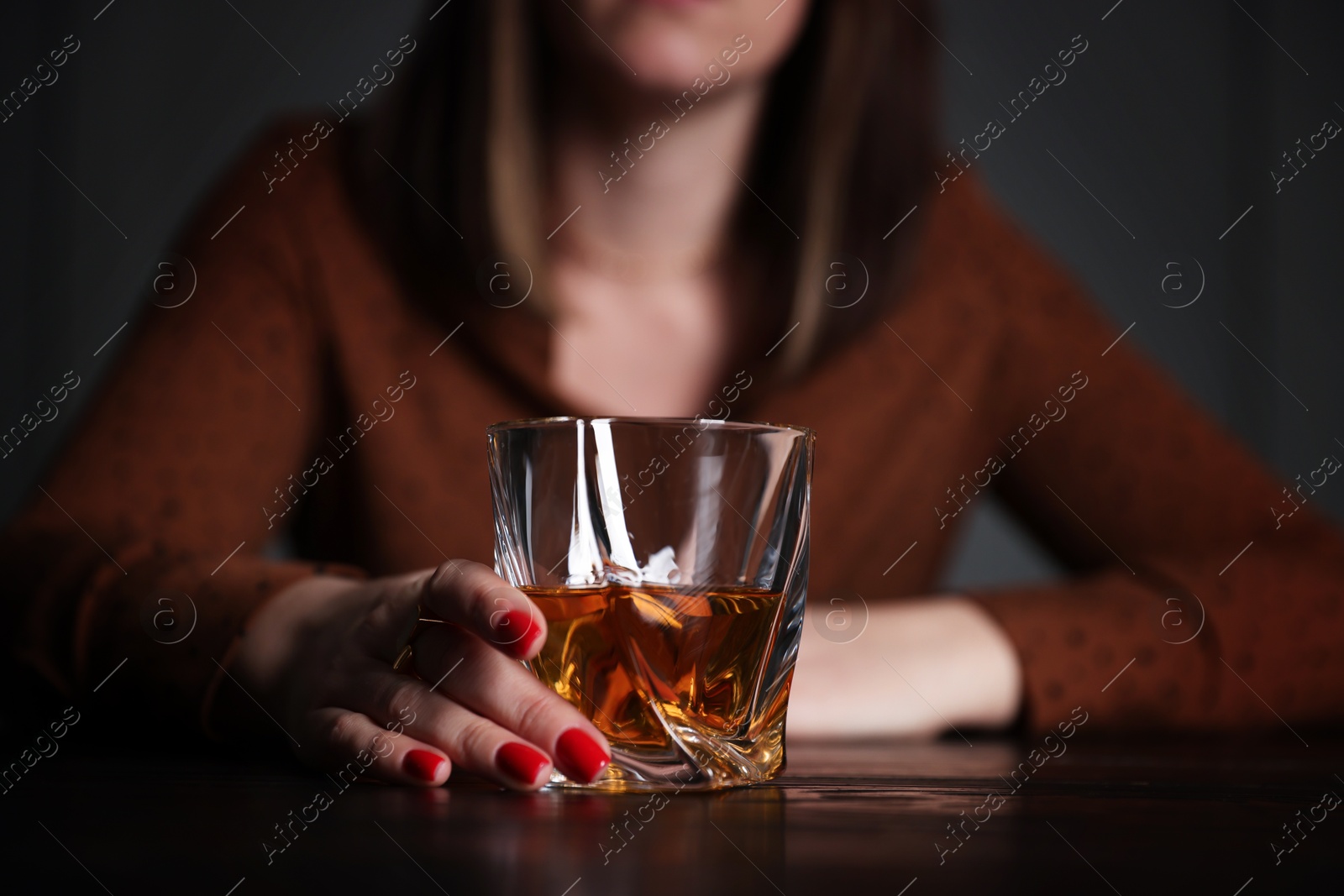 Photo of Alcohol addiction. Woman with glass of whiskey at wooden table indoors, closeup