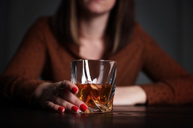 Photo of Alcohol addiction. Woman with glass of whiskey at wooden table indoors, closeup