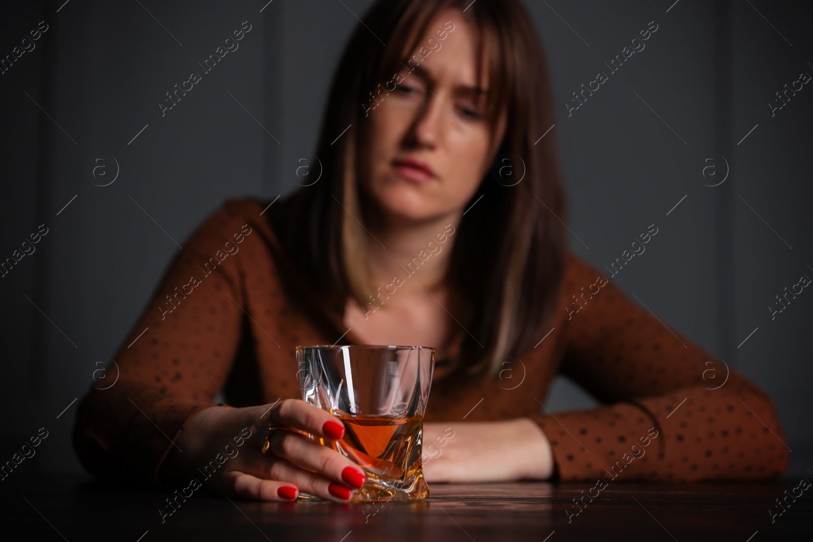 Photo of Alcohol addiction. Woman with glass of whiskey at wooden table indoors, selective focus