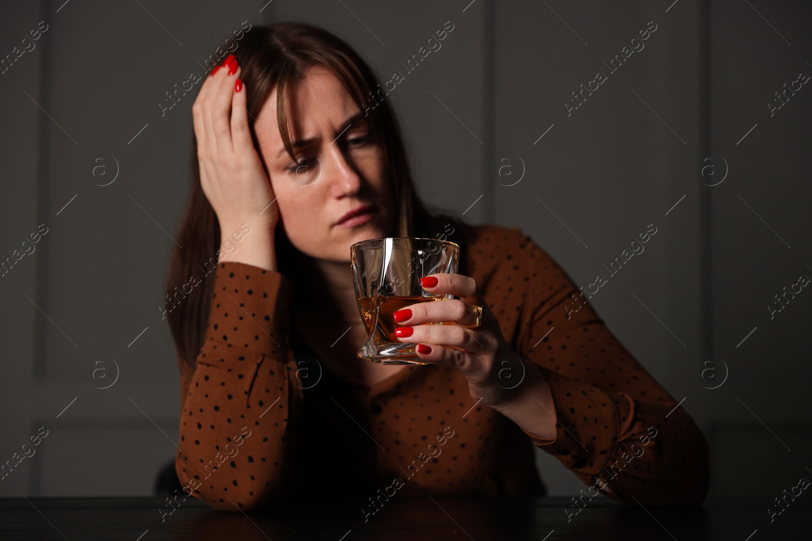 Photo of Alcohol addiction. Woman with glass of whiskey at wooden table indoors