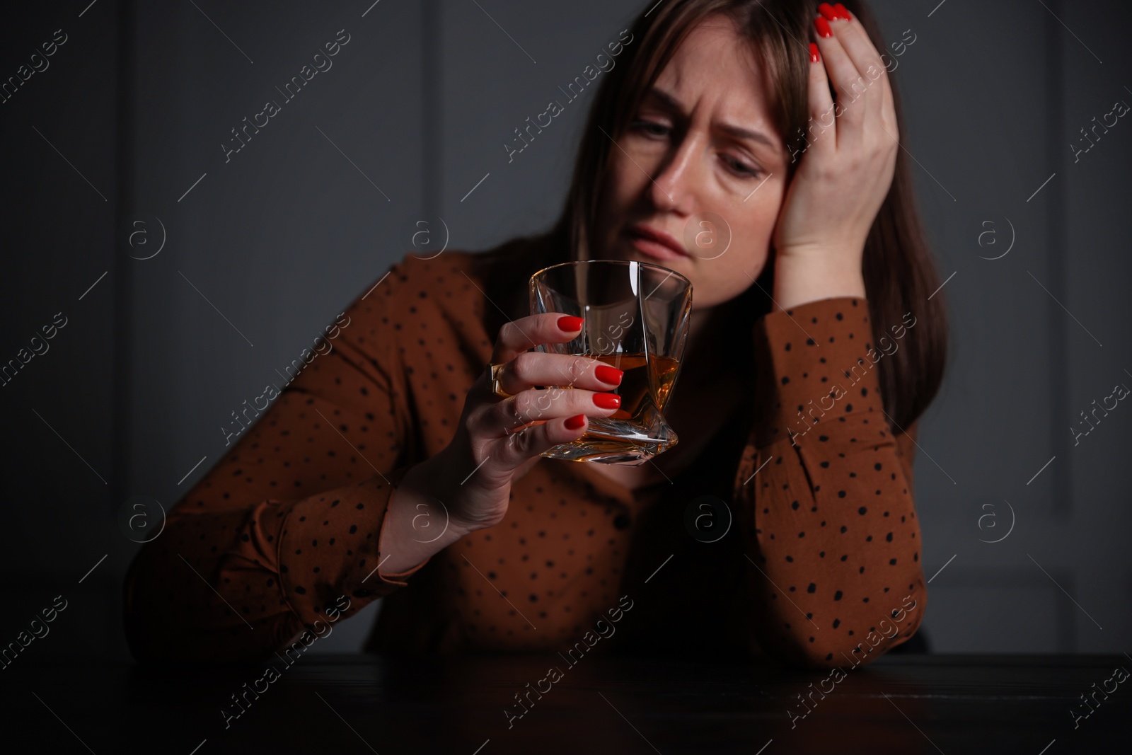 Photo of Alcohol addiction. Woman with glass of whiskey at wooden table indoors