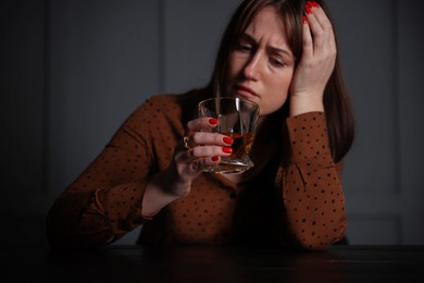 Photo of Alcohol addiction. Woman with glass of whiskey at wooden table indoors