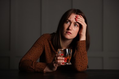 Photo of Alcohol addiction. Woman with glass of whiskey at wooden table indoors