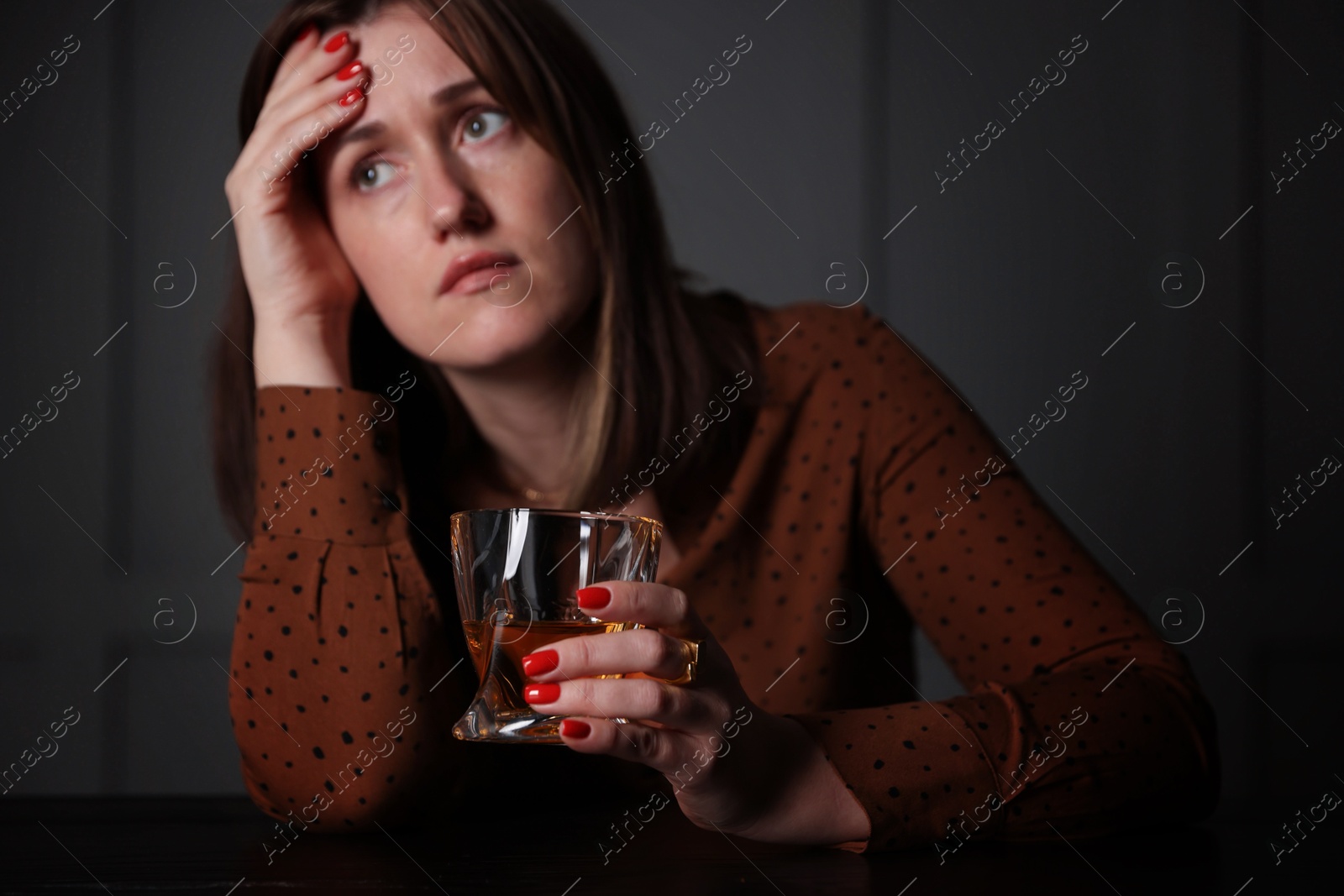 Photo of Alcohol addiction. Woman with glass of whiskey at wooden table indoors, selective focus