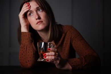 Photo of Alcohol addiction. Woman with glass of whiskey at wooden table indoors, selective focus