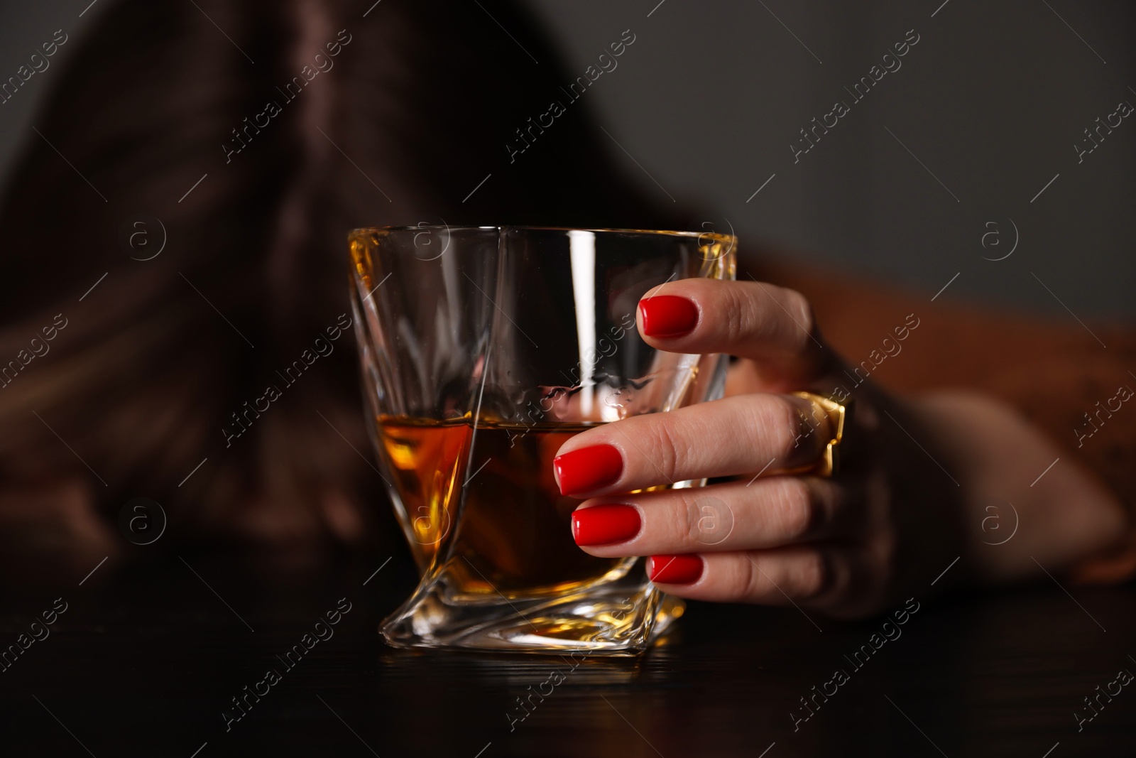 Photo of Alcohol addiction. Woman with glass of whiskey at wooden table indoors, selective focus