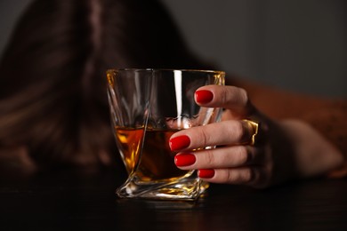 Photo of Alcohol addiction. Woman with glass of whiskey at wooden table indoors, selective focus