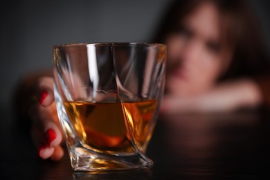 Photo of Alcohol addiction. Woman with glass of whiskey at wooden table indoors, selective focus