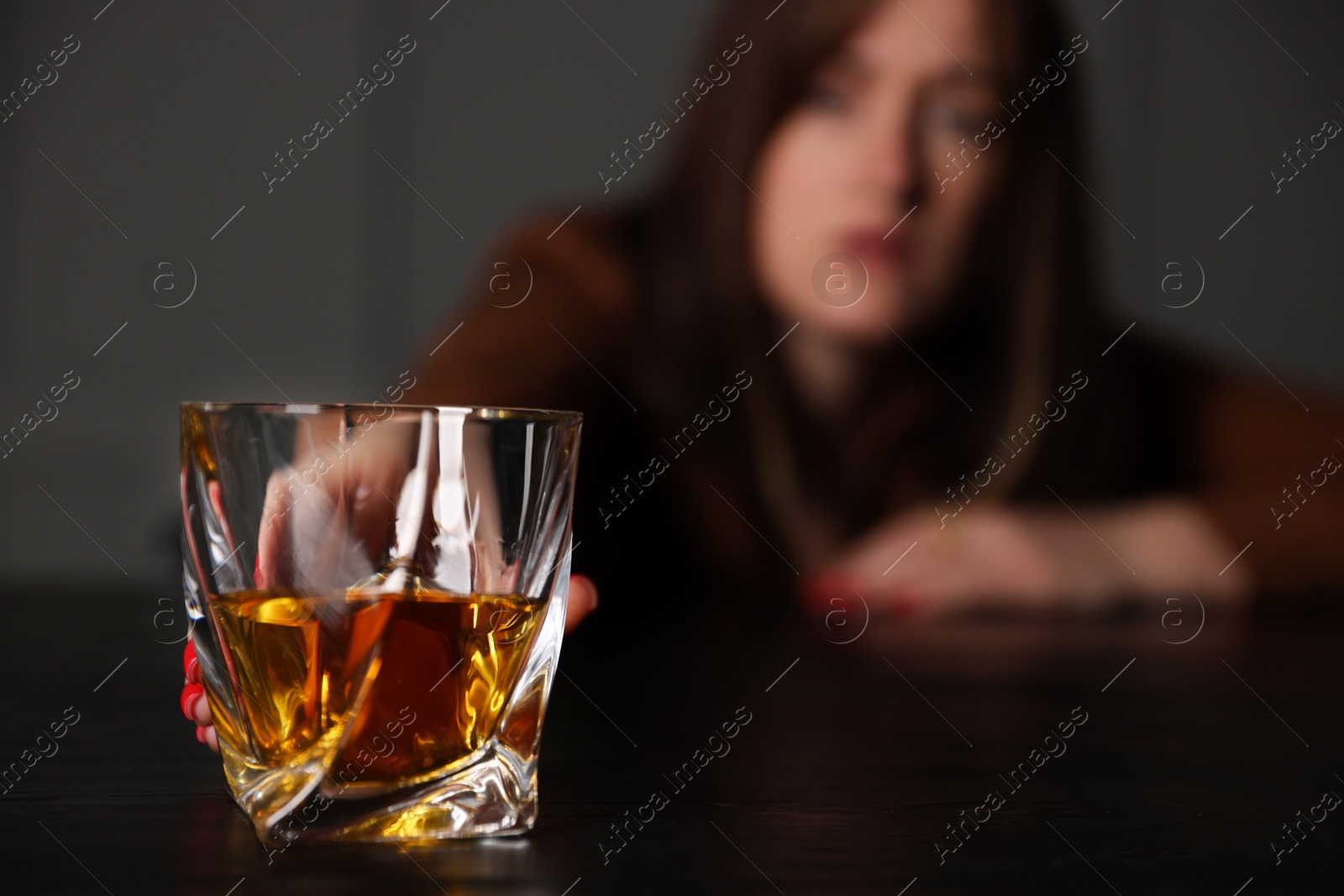 Photo of Alcohol addiction. Woman with glass of whiskey at wooden table indoors, selective focus