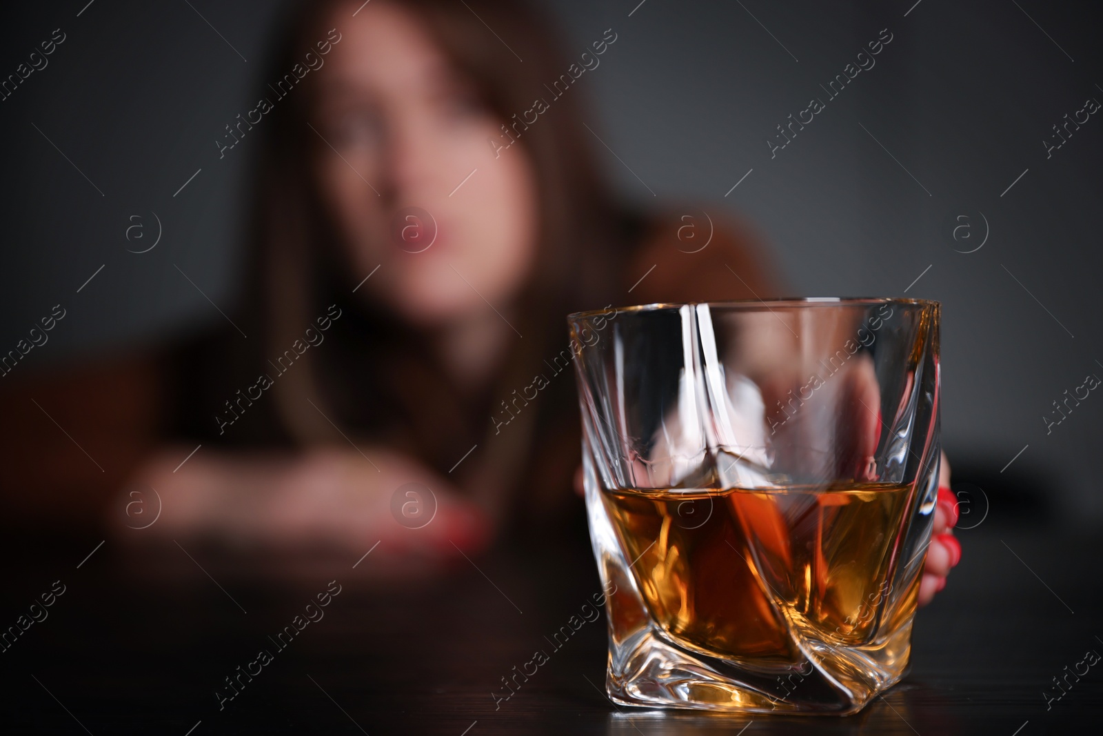 Photo of Alcohol addiction. Woman with glass of whiskey at wooden table indoors, selective focus