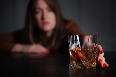 Photo of Alcohol addiction. Woman with glass of whiskey at wooden table indoors, selective focus