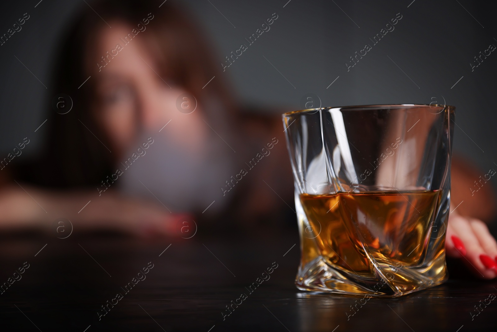 Photo of Alcohol addiction. Woman with glass of whiskey at wooden table indoors, selective focus