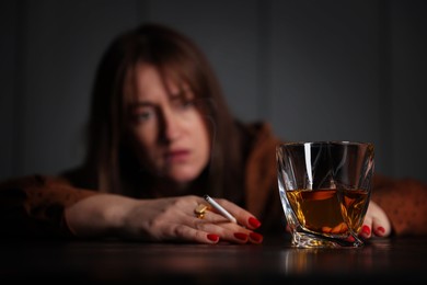 Photo of Alcohol addiction. Woman with glass of whiskey and cigarette at table indoors, selective focus