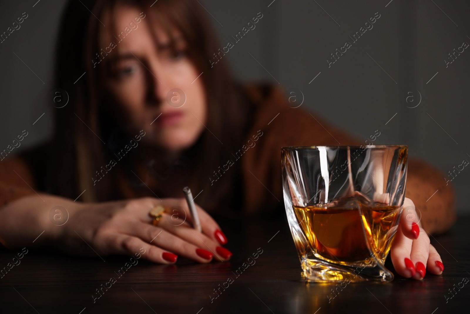 Photo of Alcohol addiction. Woman with glass of whiskey and cigarette at table indoors, selective focus