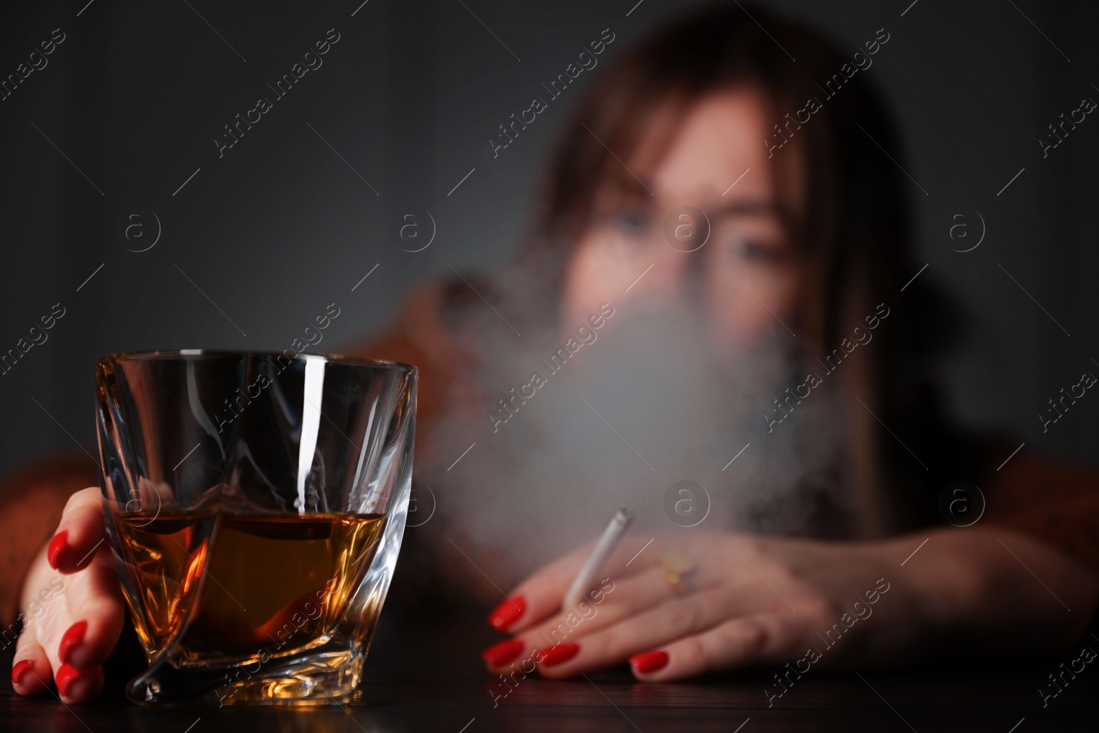 Photo of Alcohol addiction. Woman with glass of whiskey and cigarette at table indoors, selective focus