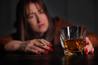 Photo of Alcohol addiction. Woman with glass of whiskey and cigarette at table indoors, selective focus